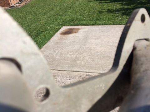 1973 Ford F-100 - A close-up, out-of-focus shot shows a metal part in the foreground, with a concrete patio and green grass in the background. A dark stain i…