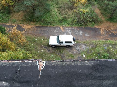 1993 Ford Bronco - An overhead view shows a white 1993 Ford Bronco parked on a dirt and asphalt road surrounded by trees and overgrown grass. The vehicle has…