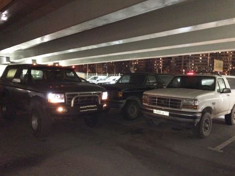 1993 Ford Bronco - Two Ford Bronco SUVs are parked under an overpass at night. The Bronco on the left is dark colored and the Bronco on the right is white.