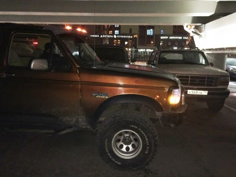 1993 Ford Bronco - A brown Ford Bronco is parked next to a white Ford Bronco under an overhang at night. The brown Bronco is in the foreground, showing its fr…