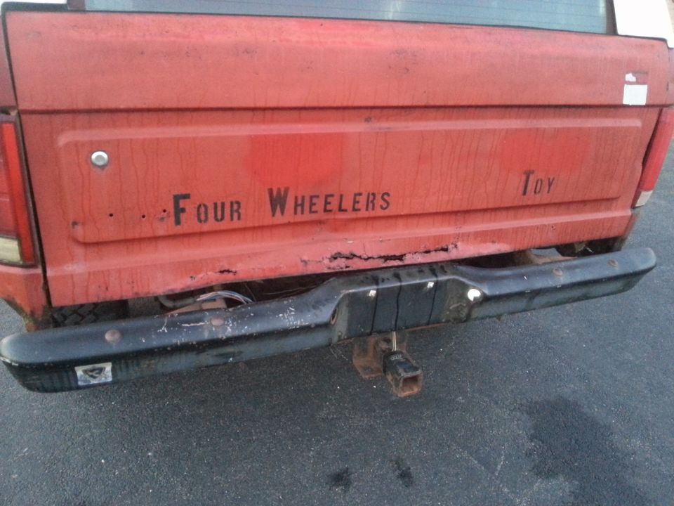 Rear tailgate of a red Ford truck reading Four Wheelers Toy with rear bumper