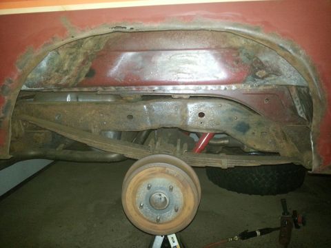 1984 Ford Bronco - Photo of a rusty front frame crossmember and brake drum on the underside of a red vehicle.