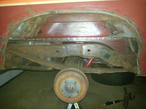 1984 Ford Bronco - Photo of a rusty front frame crossmember and brake drum on the underside of a red vehicle.
