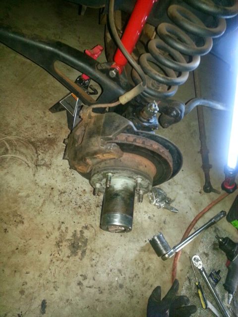 1984 Ford Bronco - Photo of a front brake rotor, spindle, coil spring and red shock during disassembly.