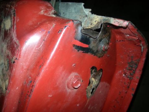 1984 Ford Bronco - Photo of a red sheet-metal body panel corner with chipped paint and rust damage.