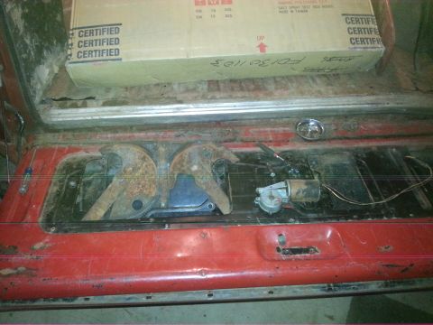 1984 Ford Bronco - Photo of an open red tailgate with latch and linkage hardware; a marked cardboard box sits behind.