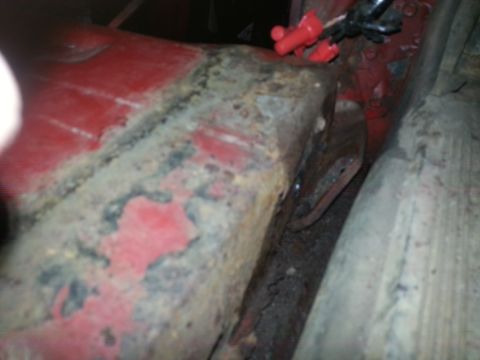 1984 Ford Bronco - Photograph of a corroded truck cab corner and rocker area under a vehicle, not a technical document.