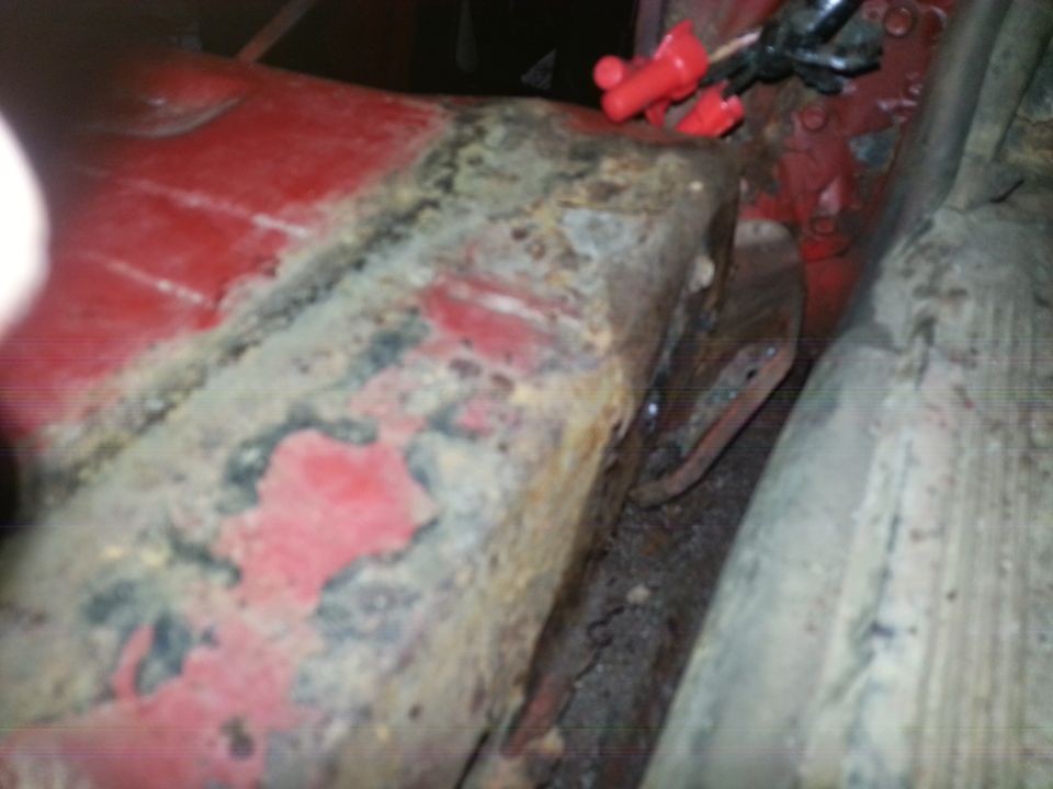 Photo of a rusty truck cab corner and rocker panel with red paint