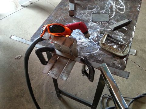 1984 Ford Bronco - Photo of cut sheet-metal pieces, a plasma cutter, and C-clamps on a steel fabrication table.