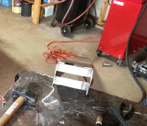 1984 Ford Bronco - Photo of a welded sheet-metal bracket on a fabrication table next to shop equipment.