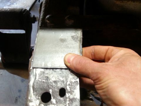 1984 Ford Bronco - Photo of a hand holding a freshly welded sheet-metal bracket with drilled holes.