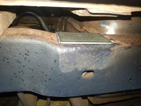 1984 Ford Bronco - Photo of a vehicle undercarriage showing a painted frame section and a small metal access plate, not a document.