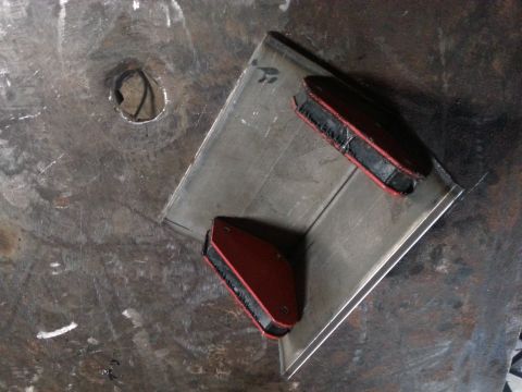 1984 Ford Bronco - Photo of a fabricated metal bracket positioned with magnetic welding clamps on a workbench, not a document.