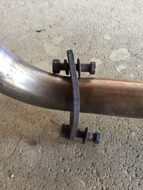 1984 Ford Bronco - Photo of an exhaust pipe secured by a bolted hanger clamp on a concrete floor, not a document.