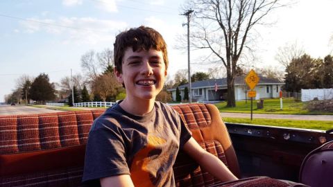 1984 Ford Bronco - Photo of a smiling young person seated in a vehicle along a rural road, not a document.
