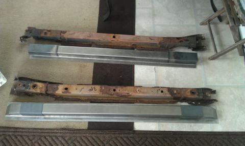 1984 Ford Bronco - Photo of rusted vehicle rails laid out next to new replacement metal sections on a floor, not a document.