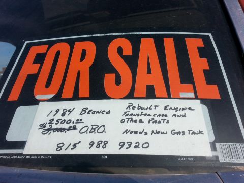1984 Ford Bronco - Photo of a handwritten For Sale window sign listing a 1984 Bronco with rebuilt engine and phone number, not a technical document.