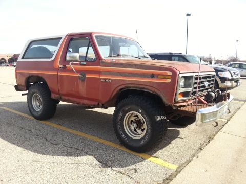 1984 Ford Bronco - Photo of a red and white 1980s Ford Bronco with a front winch parked in a lot, not a document.