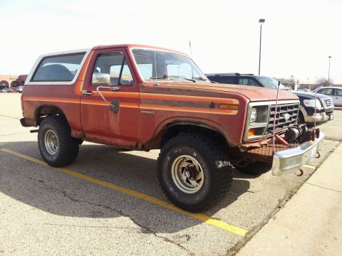 1984 Ford Bronco - Photo of a red and white 1980s Ford Bronco with a front winch parked in a lot, not a document.