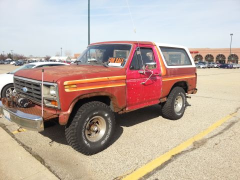 1984 Ford Bronco - Photo of a red and white Ford Bronco displaying a For Sale sign in a parking lot, not a document.