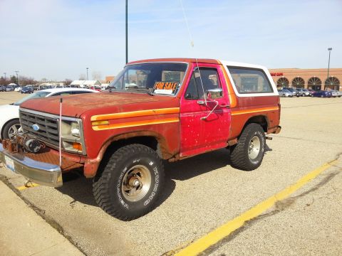 1984 Ford Bronco - Photo of a red and white Ford Bronco displaying a For Sale sign in a parking lot, not a document.