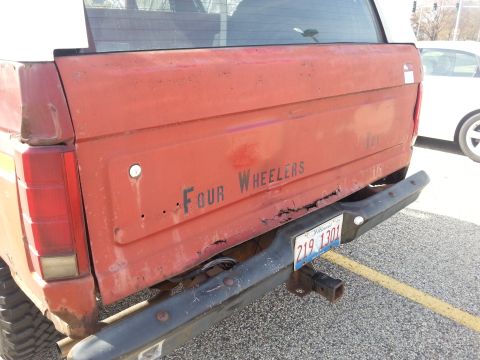 1984 Ford Bronco - Photo of a red truck tailgate lettered Four Wheelers above a rear bumper and hitch, not a document.