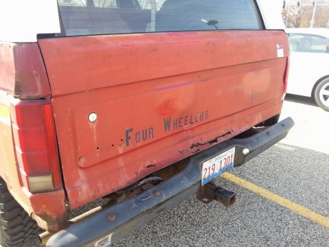 1984 Ford Bronco - Photo of a red truck tailgate lettered Four Wheelers above a rear bumper and hitch, not a document.