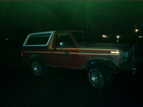 1984 Ford Bronco - Nighttime photograph of a red Ford Bronco in profile, not a document.