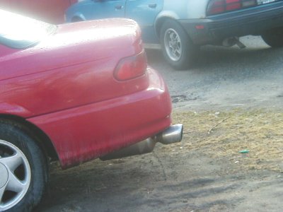 1997 Ford Taurus - A red sedan is parked next to another vehicle, showing its rear bumper and exhaust pipe.