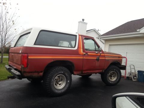 1984 Ford Bronco - Photograph of a red Ford Bronco rear three-quarter view in a driveway, not a document.