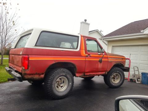 1984 Ford Bronco - Photograph of a red Ford Bronco rear three-quarter view in a driveway, not a document.