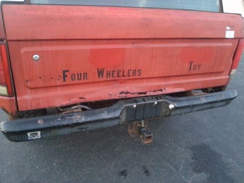 1984 Ford Bronco - Photograph of a red truck tailgate with rust and 'Four Wheelers Toy' lettering, not a document.