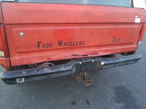 1984 Ford Bronco - Photograph of a red truck tailgate with rust and 'Four Wheelers Toy' lettering, not a document.