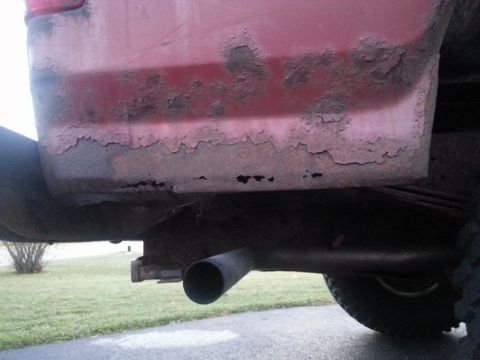 1984 Ford Bronco - Photograph of rust damage on a red vehicle's lower body near the exhaust, not a document.