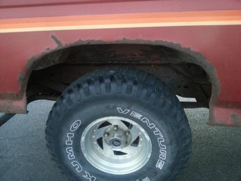 1984 Ford Bronco - Photograph of a rusted rear wheel well and tire on a red vehicle, not a document.
