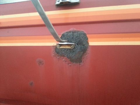 1984 Ford Bronco - Photograph of bubbling rust on a red body panel around a metal trim bracket, not a document.