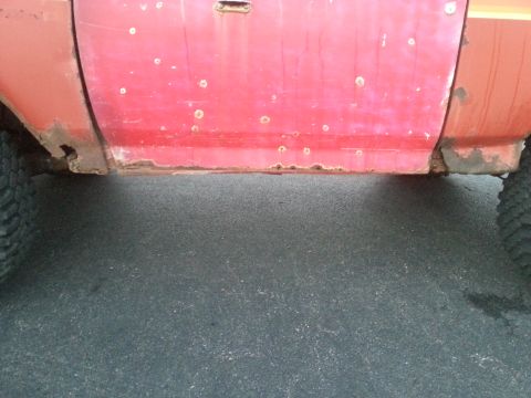 1984 Ford Bronco - Photograph of a red truck's lower door and rocker panel area, not a technical document.