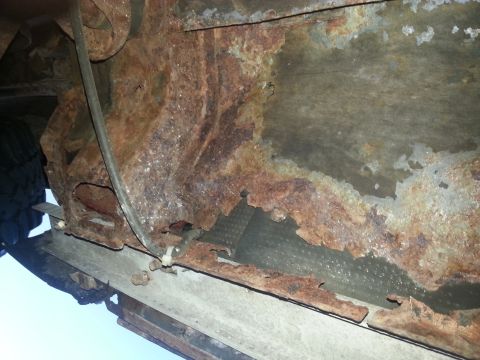 1984 Ford Bronco - Photograph of a heavily rusted floor pan and rocker viewed from beneath a vehicle, not a technical document.