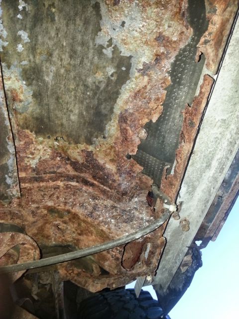 1984 Ford Bronco - Photograph of a corroded floor pan and frame area beneath a vehicle, not a technical document.
