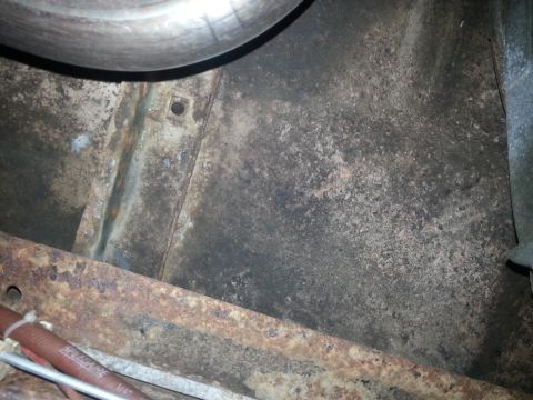 1984 Ford Bronco - Photograph of a rusty floor pan and brake drum under a vehicle, not a technical document.