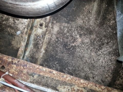 1984 Ford Bronco - Photograph of a rusty floor pan and brake drum beneath a vehicle, not a technical document.