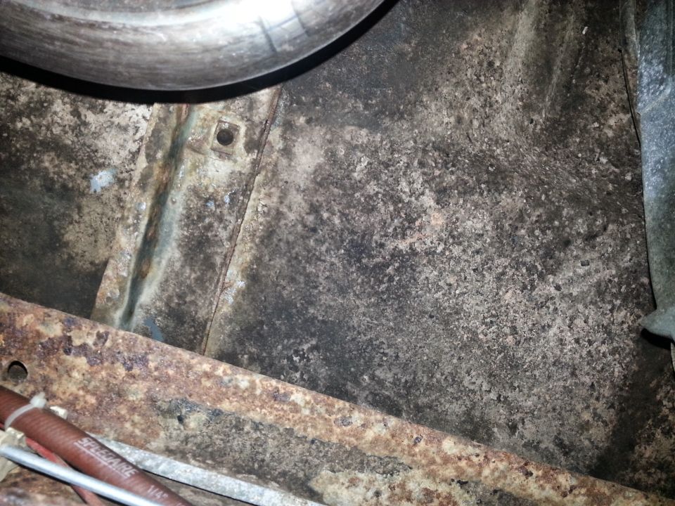 Photo of a rusted floor pan and brake drum from under a vehicle