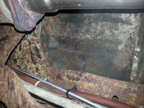 1984 Ford Bronco - Photograph of a rusted frame rail and fuel line beneath a vehicle, not a technical document.