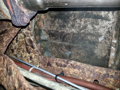 1984 Ford Bronco - Photograph of a rusted frame rail and fuel line beneath a vehicle, not a technical document.