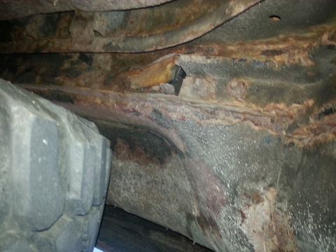 1984 Ford Bronco - Photograph of a rusted frame rail and floor structure beneath a vehicle, not a technical document.