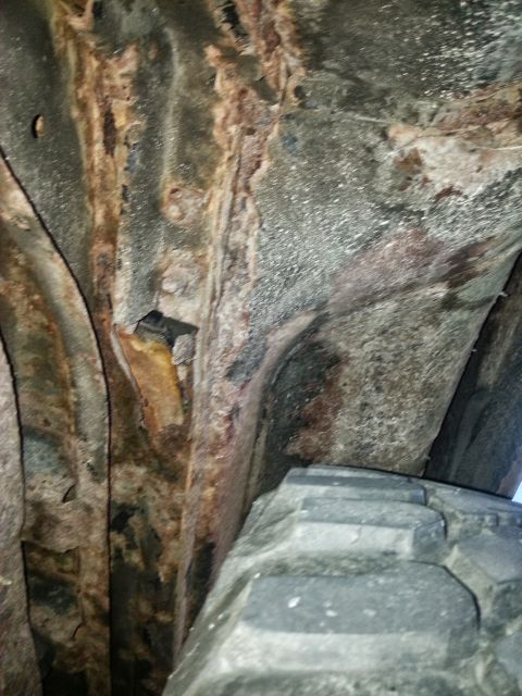 1984 Ford Bronco - Photograph of a rusted frame and rocker area beside a tire beneath a vehicle, not a technical document.