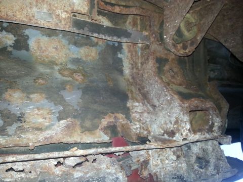 1984 Ford Bronco - Photograph of a heavily corroded floor pan and frame beneath a vehicle, not a technical document.