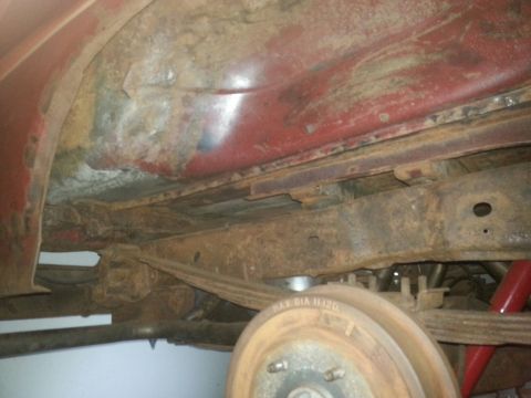 1984 Ford Bronco - Photograph of a rusted frame rail, leaf spring, and brake drum beneath a vehicle, not a technical document.