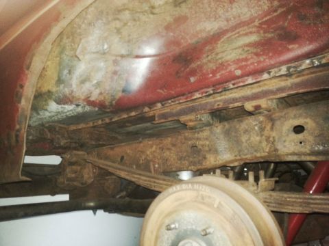 1984 Ford Bronco - Photograph of a rusted frame rail, leaf spring, and brake drum beneath a vehicle, not a technical document.