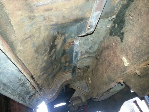 1984 Ford Bronco - Underbody photo of a vehicle floor pan and frame rail with surface rust and old undercoating, not a document.